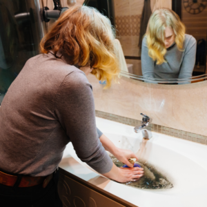 Woman trying to control overflowing water from a clogged pipe in a sink.