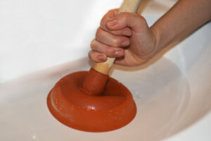 Woman with plunger trying to remove clogged sinks.