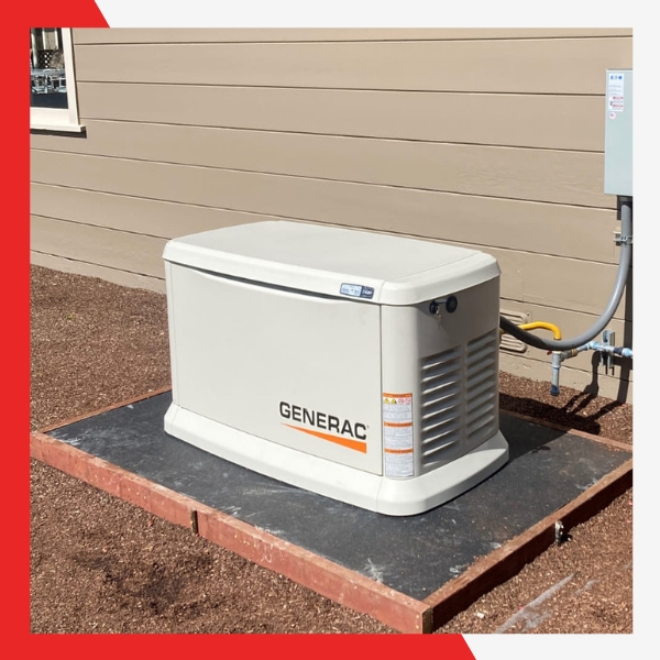 A light beige Generac home standby generator, with "GENERAC" branding, placed on a dark mat over a gravel bed with wooden borders, beside a tan house with an electrical box.