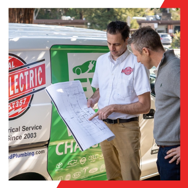 A technician in a white "Divine Electric" shirt points to a blueprint he's holding, discussing it with a male client next to a company service van.